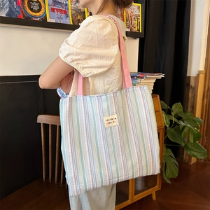 Vista dettagliata di una grande borsa tote in tela a righe indossata a spalla da una modella