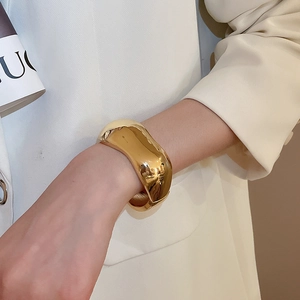 Polished gold irregular streamline wide cuff bracelet on a model wrist for fashion