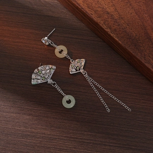 Detailed macro of fan-shaped silver tassel earrings with green ring on wood