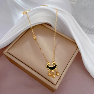 Close-up of gold titanium steel coin lock necklace with black enamel and tassel detail