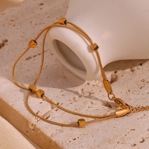 Close-up of dual-layer gold snake chain bracelet with square beads on a stone