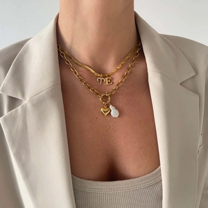 Layered gold necklaces with letter TE pendant, heart charm, and baroque pearl detail