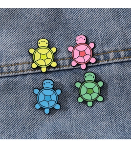 Set of four colorful enamel turtle pins in yellow, pink, blue, and green on denim