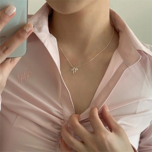 Close-up of a silver bow pendant necklace worn on neck with a minimalist style