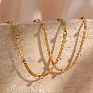 Detail of gold snake chain necklace with square clear zircon stones on marble