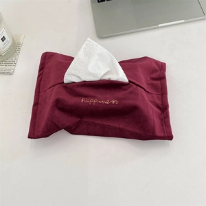 Detail of burgundy velvet tissue bag with golden Happiness embroidery on a white desk