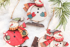 Close-up of wooden snowman ornaments on white snow with green pine branches