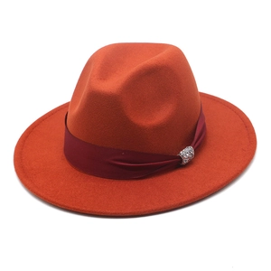 Detail of orange wool felt fedora featuring a dark red ribbon and rhinestone buckle