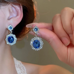 Close-up of model wearing silver halo earrings with large oval blue gemstones and diamonds