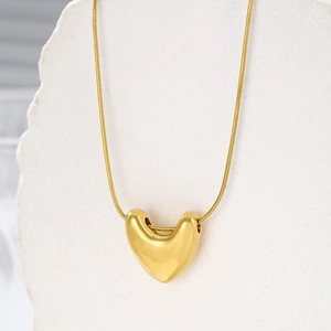 Detail of polished gold heart pendant and sleek snake chain on a textured stone stand
