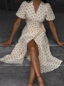 Detail view of cotton wrap dress with red heart prints and tie-waist on stone steps
