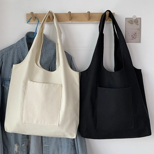 Detail of canvas tote bags in cream and black featuring a minimalist front square pocket