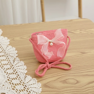 Pink straw shoulder bag for kids with white organza bow and pearl detail on wooden desk