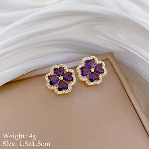Close-up of gold-plated clover earrings with purple heart stones on a jewelry box