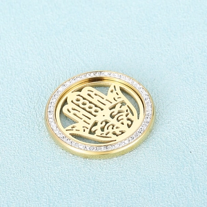 Golden Hamsa pendant with pavé crystals on a light blue textured background