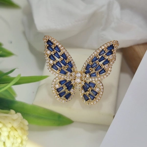 Detailed close-up of a golden butterfly ring with blue rectangular gemstones and small zircons