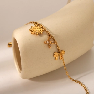 Close-up of gold-plated bracelet with sun, flower, and bow charms on ceramic stand