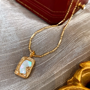Detail of gold square pendant with mother of pearl on a textured fabric background