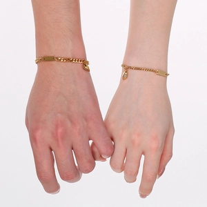 Detail of gold magnetic couple bracelets with cuban links and heart charm on wrists