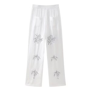 Detailed view of white wide-leg pants featuring black palm tree embroidery and elastic waist