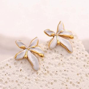 Close-up of elegant white floral stud earrings with gold plating on a white stone base