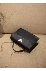 Detail of black pebbled leather mini bag featuring white butterfly clasp and gold chain