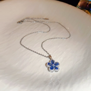 Macro detail of silver chain necklace with blue flower pendant and zircon accents