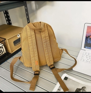 Detailansicht der Rückseite eines gelben Canvas-Rucksacks mit Riemen und Webetikett