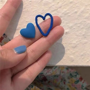 Close-up of asymmetrical matte blue heart earrings held in hand for size display