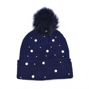 Dettaglio del berretto in maglia blu navy con perle bianche e pompon in finta pelliccia