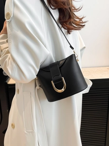 Chic black leather bucket bag with gold U-shaped buckle on white trench coat