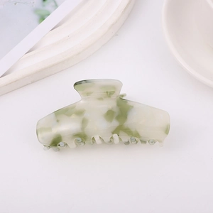 Dettaglio di un grande fermaglio per capelli in acetato con motivo marmorizzato bianco verde