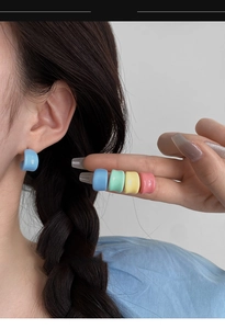 Close-up of colorful C-shaped macaron resin earrings set worn by a model in soft light