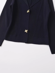 Detailed close-up of golden floral buttons and ribbed knit texture on a navy cardigan