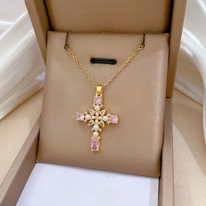 Macro shot of gold cross pendant with pink pear-shaped gem and white pearl detail