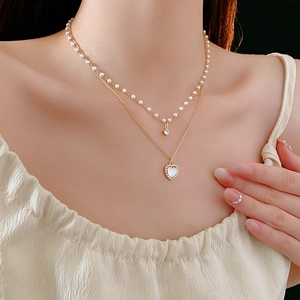 Gros plan du collier double couche doré avec pendentif en cœur et détails de perles
