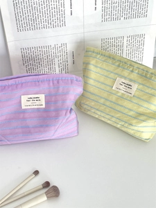 Detail view of striped canvas makeup bags in purple and green with zipper closure