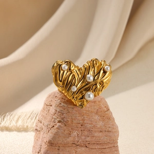 Macro shot of gold heart ring with irregular texture and inlaid pearls on rock