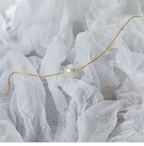 Detailed view of a single creamy pearl on a minimalist 18K gold-plated titanium chain