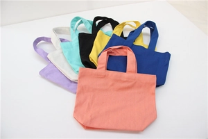 Close-up of colorful canvas lunch bags in pink, blue, yellow and green stacked in a fan layout