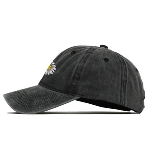 Detail of embroidered daisy on washed black cotton baseball cap with vintage finish