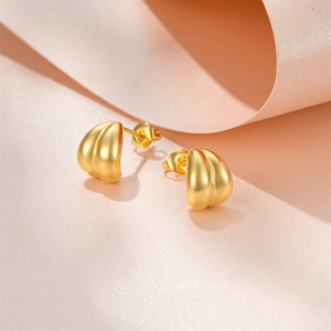 Detail of gold matte heart stud earrings with textured finish on curved background