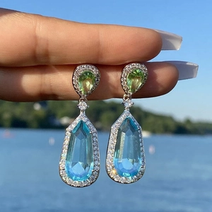 Detail of tear-drop earrings featuring blue and green gemstones with pavé borders