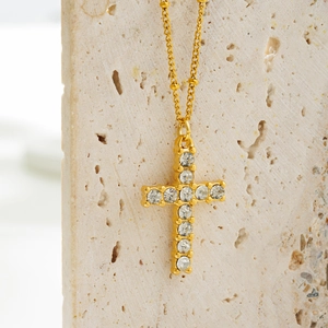 Detailed close-up of golden cross necklace with clear rhinestones on textured stone base