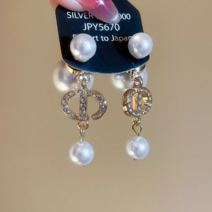 Detailed view of gold-plated pearl drop earrings featuring a sparkling zircon CD logo