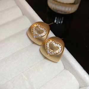 Vue macro de boucles d'oreilles cœur en or mat serties de cristaux sur velours blanc