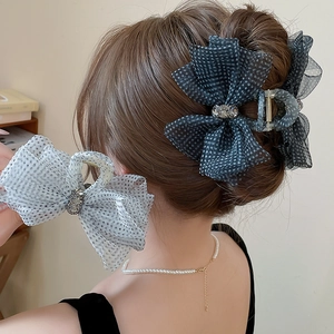 Detail showing a large navy blue mesh bow hair claw clip with white polka dots and rhinestones