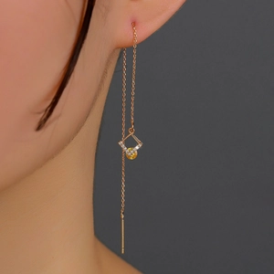 Close-up of gold thread earring with square zircon pendant and yellow gemstone on ear