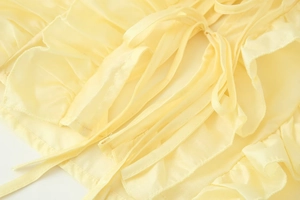 Dettaglio del tessuto plissettato giallo con lacci e maniche a balze graduate