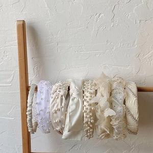 Collection of white pearl and lace bow headbands displayed on a wooden stand